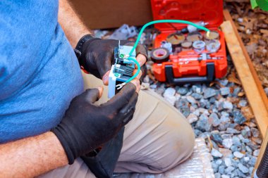 İşçi inşaat alanındaki çakıl araçlarının yanında yerde otururken elektrik parçalarıyla ilgilenir