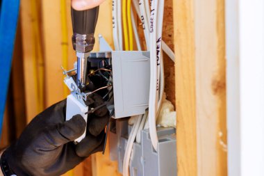 Konut ortamında elektrik panelinin içindeki kabloları bağlamak için tornavida kullanan bir elektrikçi..