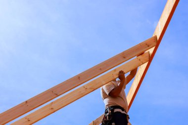 İşçi çatı kirişlerini bir araya getirmek için ahşap kirişleri kaldırıyor.