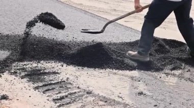 İnşaat işçisi pürüzsüz bir şekilde bitirmek için yeni yola asfalt seriyor