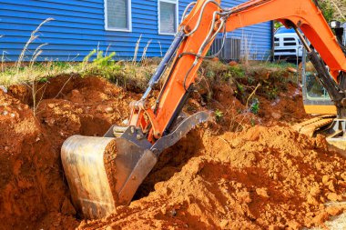 Bir kazıcı inşaat alanının yanındaki eve çukur kazmaya çalışıyor.