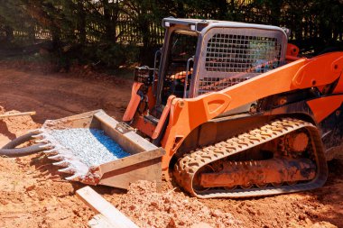 Ağır kazıcılar inşaat alanında çalışıyor. Yerleşim yerlerinde yükleyiciyle çakıl taşıyorlar..