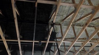 İnşaat işçileri tavandaki kirişlere köpük yalıtımı püskürterek siyah boya sıkarlar..