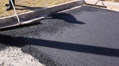 İşçiler inşaat alanında yol onarımı için yere sıcak asfalt yaymak için araçlar kullanıyorlar