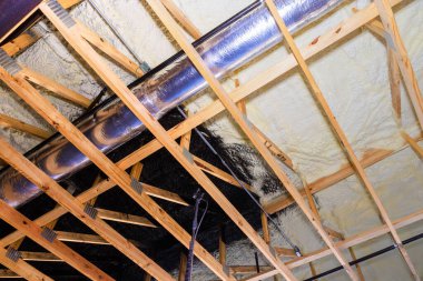 İnşaat işçileri tavandaki kirişlere köpük yalıtımı püskürterek siyah boya sıkarlar..