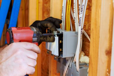 Bir elektrikçi yeni inşa edilen evin duvarına devre kesici yerleştirmek için elektrikli alet kullanıyor.