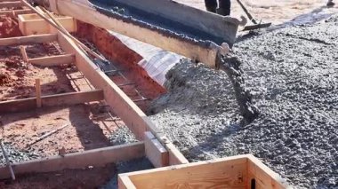İnşaat işçileri, yerleşim alanındaki yeni temel kaplaması için ahşap formlara taze beton döküyorlar.