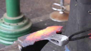 Zanaatkar, balta yapımı sırasında geleneksel demircilik sergilenirken örs üzerinde ısıtılmış metali ustalıkla çekiçliyor.