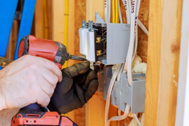 Elektrik işçisi ev onarımında devre kesici takmak için matkap kullanıyor.