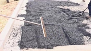 İnşaat işçileri yol yapımında kullanılan araçları kullanarak yol yüzeyine taze asfalt sürerler.