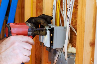 Bir elektrikçi yeni inşa edilen evin duvarına devre kesici yerleştirmek için elektrikli alet kullanıyor.