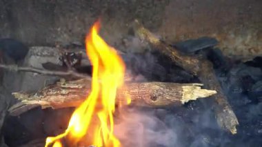 Dışarıdaki ızgarada yanan tahta çubuklarda ateş parlak bir şekilde yanıyor. İnsanlar yemek yemek için toplandıkça duman havaya yükseliyor.