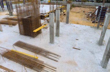 Çelik çubuklar yere serilirken, beton sütunlar açık bir alanda inşaat faaliyetleri için inşaat sahasında sabit duruyorlar..