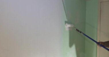 İşçi uzun saplı boya rulosuyla duvarlara boya sürerek kısmen boyanmış duvar kapılarını boyuyor..