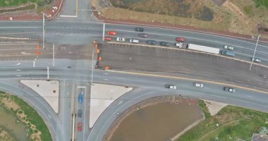 Araçlar trafik ışıklarıyla dolu bir kavşakta yol alırlar. Birkaç kamyon geçitte beklerken arabalar farklı yönlere hareket ediyor. Konum kentsel gelişimi ve yolları gösteriyor.