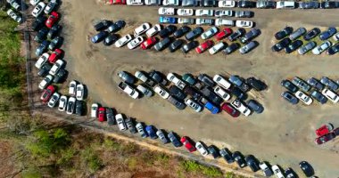 Birçok araba büyük bir alana park edilmiş. Ağaçlara yakın. Bazı boşluklar dolu, diğerleri ise boş..