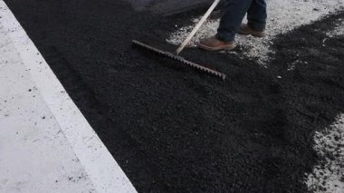 Müteahhit yol kenarındaki inşaat sahasına asfalt serpmek için tırmık kullanıyor.