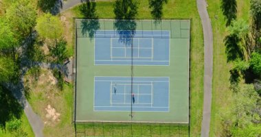 Park yollarındaki mavi kortlarda tenis oynayan iki kişi, mahkemelerin yanında koşuyor..
