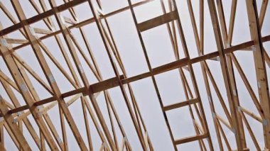 Workers create framework for joins roof using wooden beams while at building site.