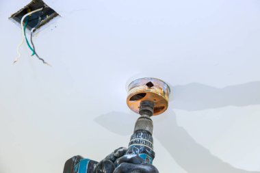 İşçi tavan armatürünü delmek için matkap kullanırken kablolar yukarıda odada asılı duruyor..