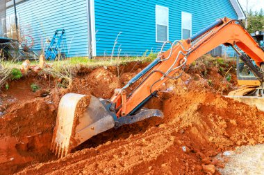 Kazıcı inşaat alanındaki evin yanındaki kırmızı toprakta derin bir çukur kazmaya çalışıyor.