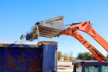 İnşaat aracı, yol çalışmaları sırasında mavi çöp konteynırına atık döker.