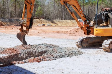 Bir kazıcı inşaat sahasında toprak kayaları kaldırarak temel oluşturur.