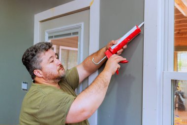 Marangoz, duvarın çerçevesini caulk ile kapatmaya çalışıyor.