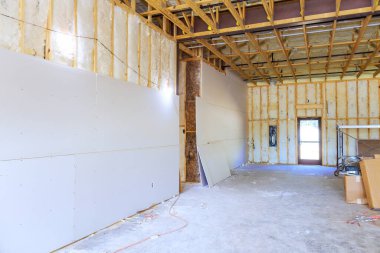 İşçiler, küçük kasabadaki yeni inşaat evine yalıtım malzemesi yerleştirdikten sonra duvarlara alçıpan yerleştiriyorlar.