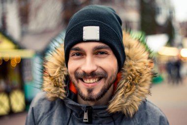 Genç, yakışıklı, gülümseyen, ağzı açık beyaz dişli, son moda sakallı, kameraya bakan adamın portresini yakından çek. Yeni yıl Noel süsleri, Sevgililer Günü konsepti.