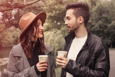 Heteroseksüel bir çiftin portresi. Bulutlu, yağmurlu, karamsar bir havada parkta dikiliyor. Birlikte vakit geçiriyor, eğleniyor, konuşuyor ve sıcak çay içiyor. Botanik bahçesinde romantik randevular.