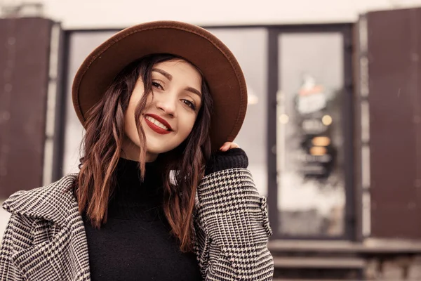 近くのストリートカフェレストランの外に立っている魅力的な女性のショットを閉じる茶色の帽子グレーのコートのポロネック黒のセーターを着て カメラを見てください 女の子は秋の春 寒さの新鮮な空気を過ごす — ストック写真