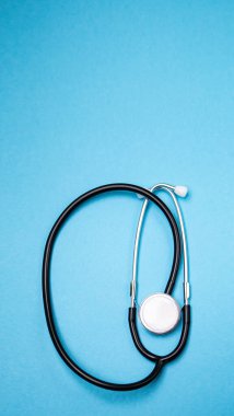 Dikey görüntü siyah modern steteskop. Mavi arka planda yansıması ve kopyalama alanı var. Tek kullanımlık maske. Tıbbi hemşire ya da doktor ekipmanı objesi. Tıp sağlık hizmetleri kavramı.
