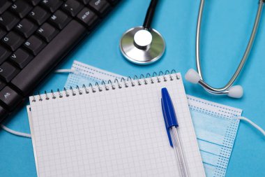 Siyah modern steteskopu mavi arka planda yansıması olan fotokopi alanı ile kapatın. Tek kullanımlık maske. Tıbbi hemşire ya da doktor ekipmanı objesi. Sağlık sigortası konsepti. Not Defteri