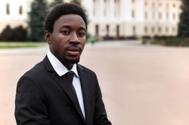 Sokakta dikilip kameraya bakan Afro-Amerikan genç iş adamının portresini yakından çek. Takım elbiseli siyah erkek ve beyaz gömlekli kravat. Kopyalama alanı olan resim.