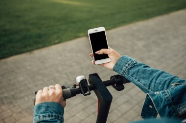 Şehrin caddesinde duran elektrikli scooterlı kadın. self-servis sokak taşımacılık kiralama servisi. Akıllı telefon uygulaması olan kentsel çevre dostu enerji aracı kiralayın.