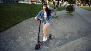 Şehrin caddesinde duran elektrikli scooterlı gülümseyen kadının portresi. self-servis sokak taşımacılık kiralama servisi. Kentsel çevre dostu enerji aracı kirala. 