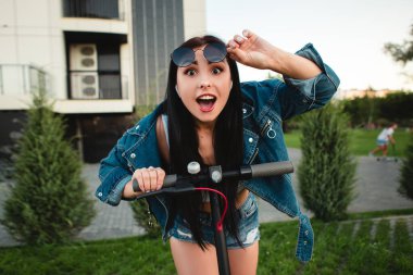 Gülümseme portresi, şehrin caddesinde duran elektrikli scooterlı, ağzı açık, ağzı açık kadını şaşırttı. self-servis sokak taşımacılık kiralama servisi. Kentsel çevre dostu kirala. 