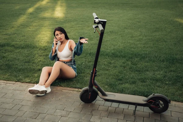 Şehrin caddesinde duran elektrikli scooterlı kadın portresi. self-servis sokak taşımacılık kiralama servisi. Akıllı telefon uygulaması olan kentsel çevre dostu enerji aracı kiralayın. 