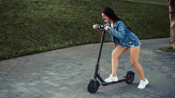 Şehrin caddesinde duran elektrikli scooterlı kadın portresi. self-servis sokak taşımacılık kiralama servisi. Akıllı telefon uygulaması olan kentsel çevre dostu enerji aracı kiralayın. 