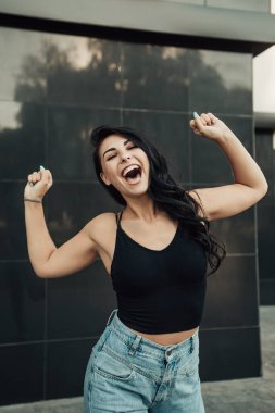 Heyecanlı, genç ve şehvetli bir kadının çığlıklarının dikey portresi. Bayan sevinçten kollarını kaldırıyor, yüksek sesle bağırıyor, cübbe ve kot pantolon giyiyor. Kopyalama alanı olan resim. Kutlama konsepti.