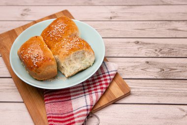 Ev yapımı yemek pişirme konsepti. Taze, yumuşak, yumuşak, zencefilli, altın sarısı, susamlı çörekler, tabak kesme tahtasındaki tatlı çörekleri. Fırın ürünleri, mutfak havlusu, kopyalama alanı.