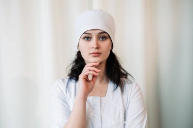 Hemşire genç doktor beyaz duvarın yanında durup kameraya bakıyor. Tıbbi önlük ve cerrahi şapka giymiş kadın doktor. Kopyalama alanı olan resim. Pandemik virüs koronavirüs konsepti
