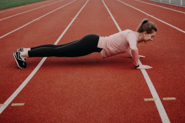 Koşu bandında şınav çeken kız. Şehir stadyumunda kardiyo eğitimi. İş gününden önce sabah ısınması. Bir kadın vücudunu uyarıyor. Sağlıklı yaşam biçimi, kopyalama alanı olan resim.