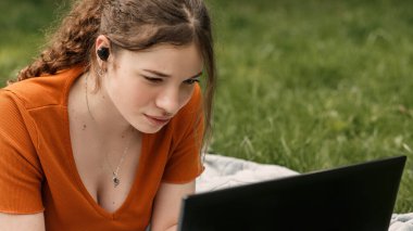 Fotokopi alanı olan mutsuz genç kız üniversite öğrencisinin yakın portresi. Yeşil çimenlerin üzerinde dizüstü bilgisayarı ve kablosuz kulaklığı olan bir kadın. Hüsrana uğramış, üzgün, kötü huylu kadın.. 