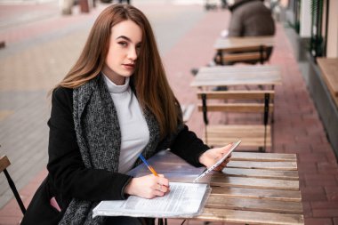 Small busy business owner elegant pretty woman office manager freelancer sitting outside street cafe coffee shop wooden table, signing documents, working with papers. Entrepreneur, copy space