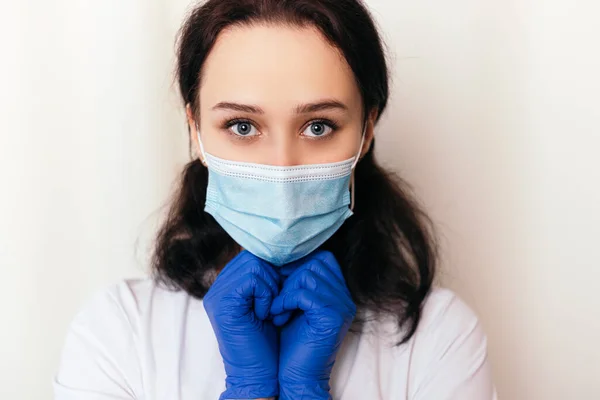 Nurse young medic with rubber disinfected gloves. Female doctor dressed in medical gown and surgical face blue mask. Image with copy space. Pandemic virus coronavirus concept