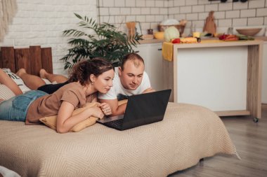 Yatakta dizüstü bilgisayar ekranına bakarak uzanan sevimli aile portresini yakından çek. Genç Avrupalı mutlu aşıklar eşleriyle evlenip internette sörf yapıyor, internetten alışveriş yapıyor ya da bilet alıyor..