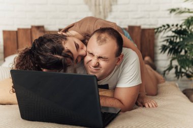 Dizüstü bilgisayarı olan ve yatakta öpüşen genç çiftin seçici odağı. Genç Avrupalı mutlu aşıklar eşleriyle evlenip internette sörf yapıyor, internetten alışveriş yapıyor ya da bilet alıyor..