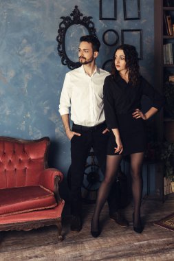 Genç çiftin dikey portresi, fotostudio veya eski apartman odasındaki antik dekorasyonların arka planında duruyor ve poz veriyor. Karı koca balayında, birlikte vakit geçiriyorlar..